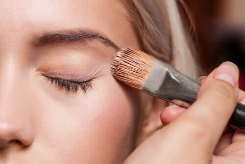Woman applying foundation to her face: makeup to correct blemishes