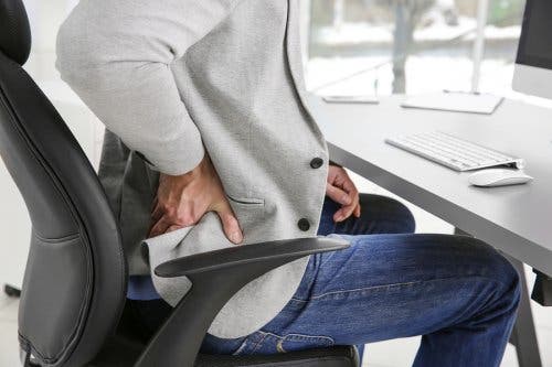 Man sitting in office chair, holding his back in pain.