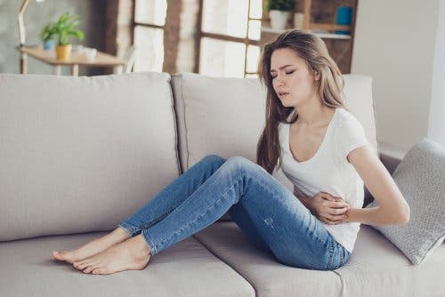 Woman on couch holding stomach in pain.