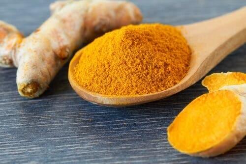 Turmeric root next to powdered turmeric on a spoon, another way to fight gallstones naturally.