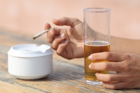 A person smoking a cigarette and drinking alcohol.