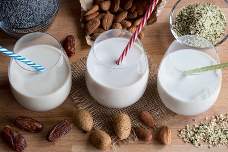 Three glasses of almond milk with different nuts around.