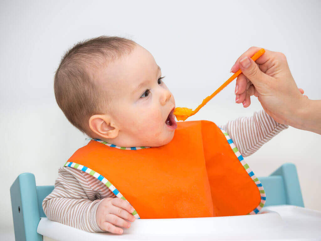 A baby eating mashed carrots.