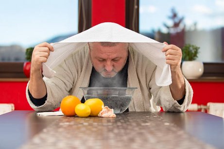 Man with towel over head inhaling steam to cure a sinus headache.