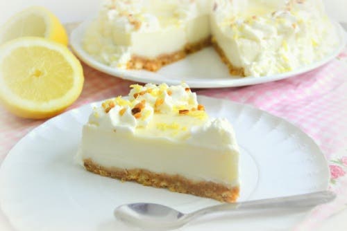 A slice of lemon meringue pie with the whole pie in the background.