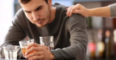 Mand drikker og kvinde lægger sin hånd på hans skulder som eksempel på, når ens partner er alkoholiker