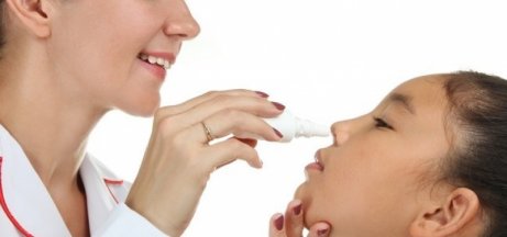 Woman spraying saline solution up girl's nose to clear sinuses.