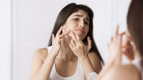 Woman squeezing acne on her face while looking in the mirror.