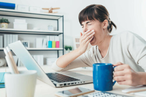 Woman with sleep inertia yawning at work in the office.