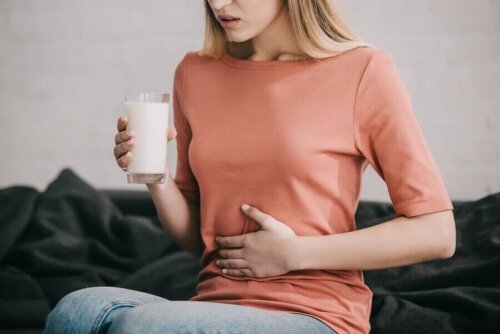 Woman holding glass of milk and stomach, lactose intolerant due to her digestive enzymes.