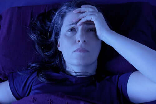 Жена лежи в леглото будна с ръка на главата си.