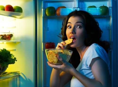 A woman eating by the fridge.