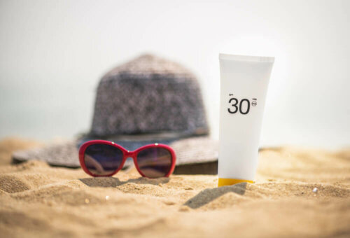 Hat, sunglasses, and sunblock tube sitting on the sand.