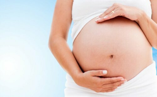 A pregnant woman in white, holding her stomach, one of the contraindications of marjoram is using it during pregnancy.
