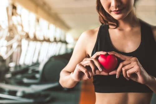 A woman at a gym holding a plastic heart in front of her chest.