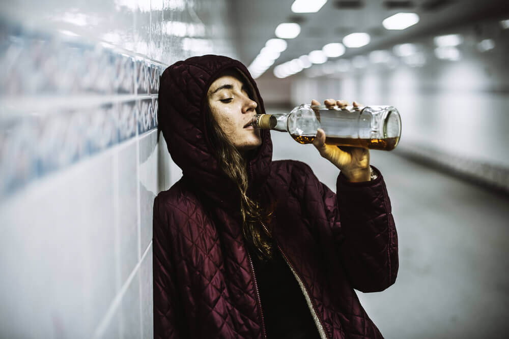 Kvinne som drikker alkohol alene på en togstasjon.