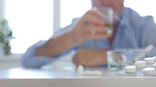 En person med en masse piller på bordet foran sig og et glas i hånden repræsenterer kombinationen af antidepressiva og alkohol
