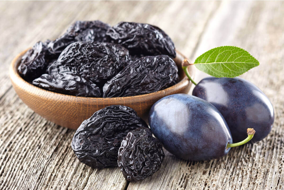 A bowl of prunes and two fresh plums.