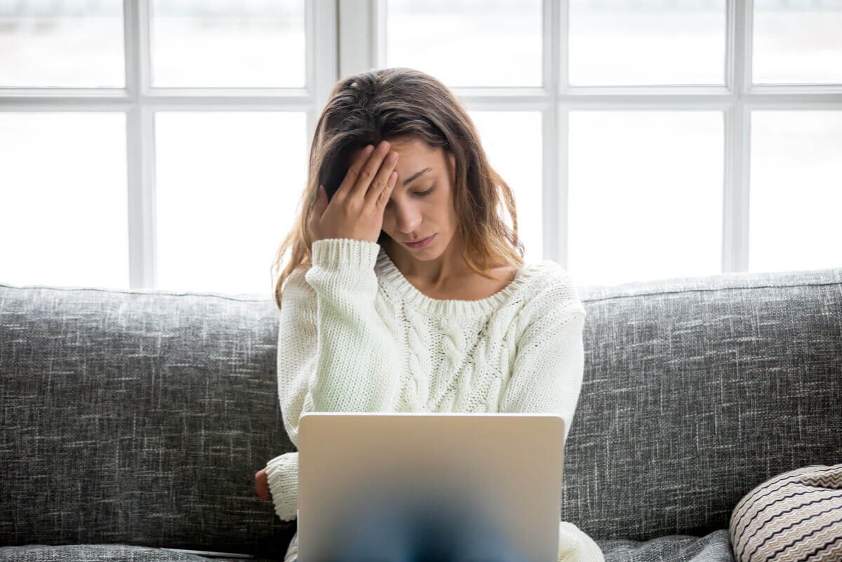 A woman experiencing stress while working on her laptop on the couch.
