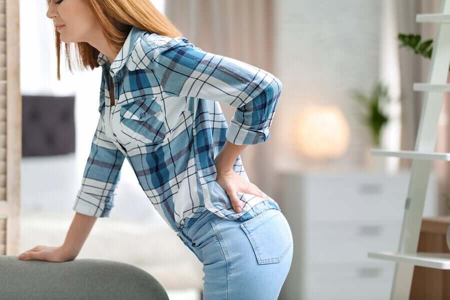 A woman bending over with her hand on her lower back.