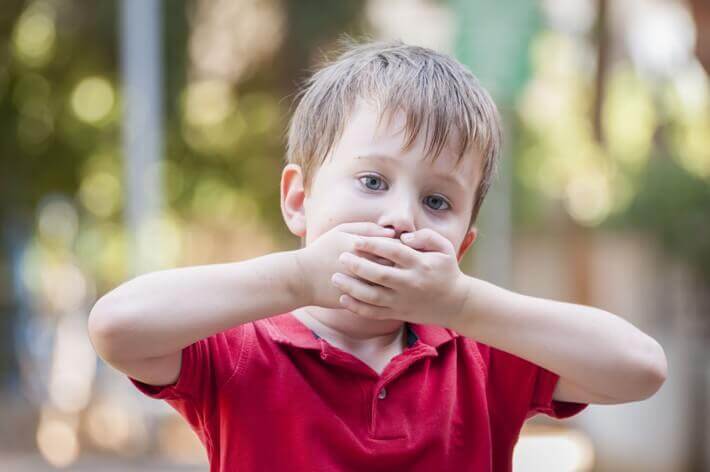 A child covering his mouth with both hands.