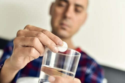 A person adding a tablet to a glass of water.
