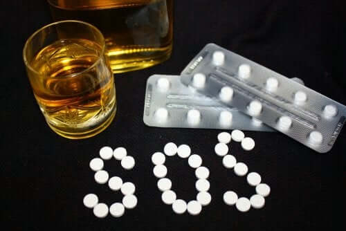 A glas with an alcoholic beverage next to blister packs of medication, and the letters S.O.S. written with pills.