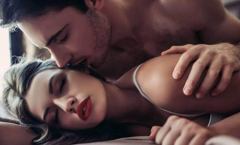 A man kissing his partner seductively while lying in bed.