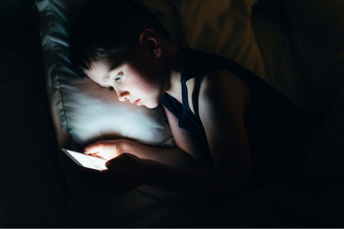 A young child looking at a tablet in bed in the dark.