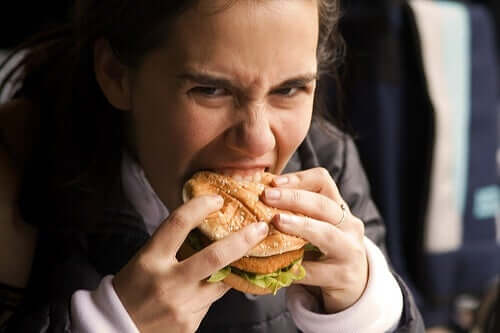 Kobieta wgryzająca się z zapałem w hamburgera. Nieodparte pragnienie jedzenia