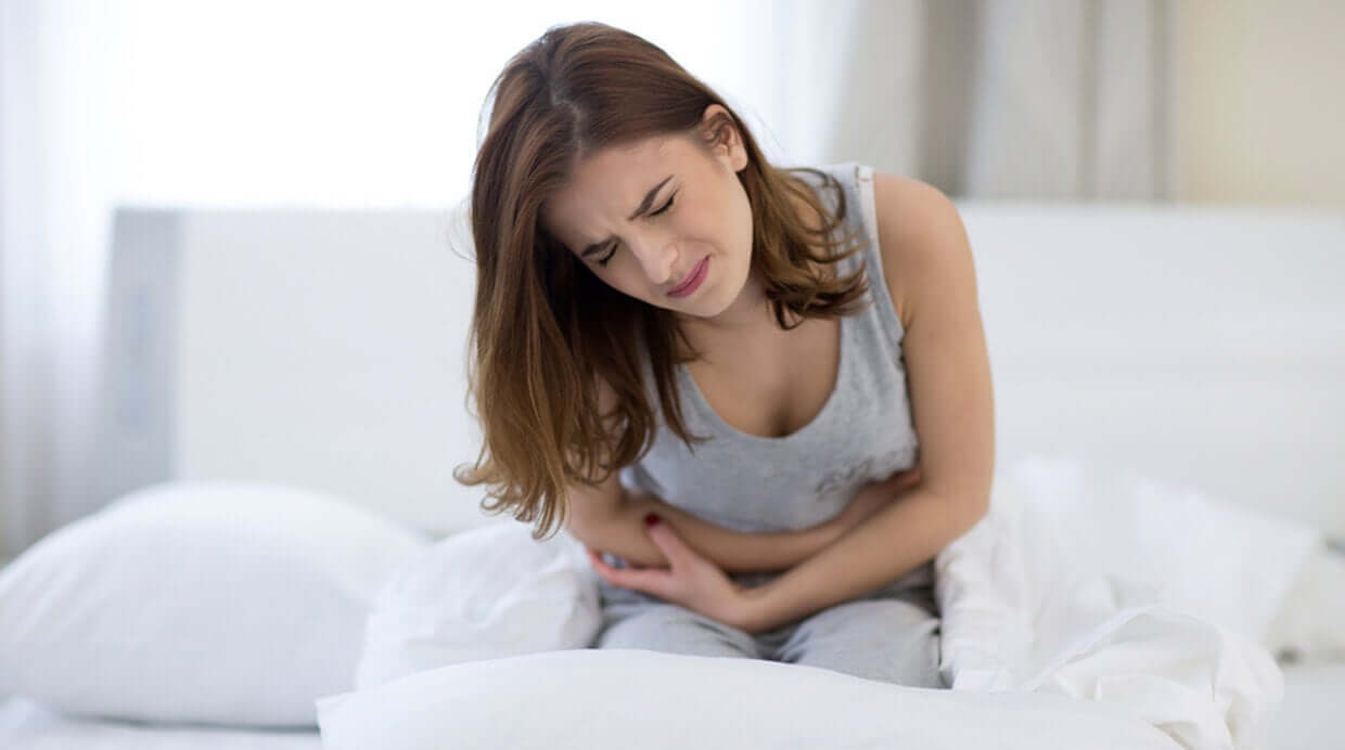 A woman double over in bed, clutching her abdomen.