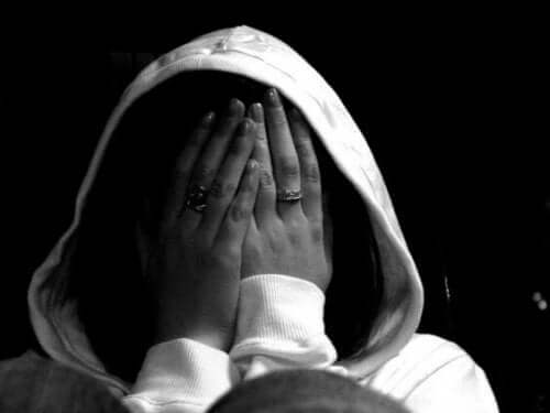 A black and white image of a woman wearing a hooded sweatshirt and covering her face with her hands.
