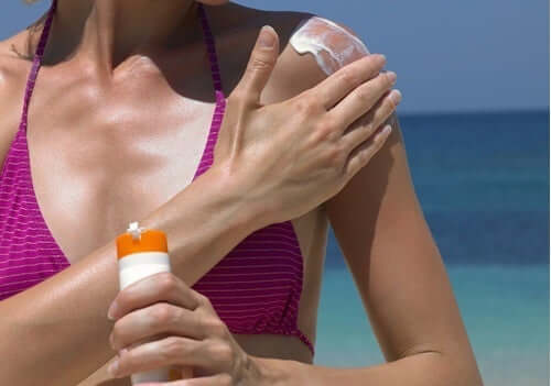A woman is enjoying a day on the beach and applying sunscreen.