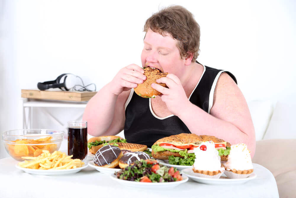 An overwieght man eating at a table full of food.