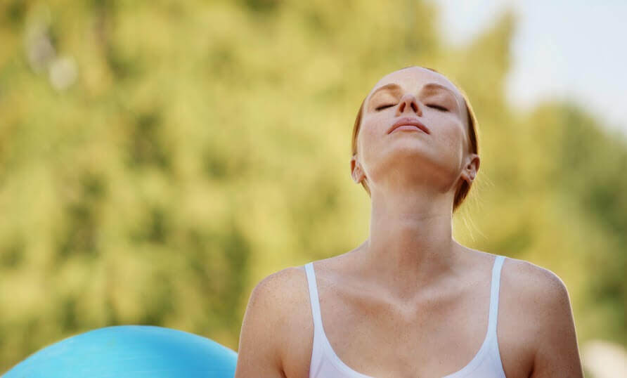A woman closing her eyes and tilting her head back while sitting near an exercise ball.