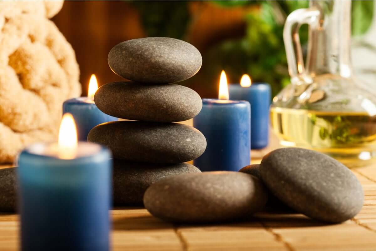 A pile of hot stones surrounded by small blue candles, spa towels, and a bottle of oil.