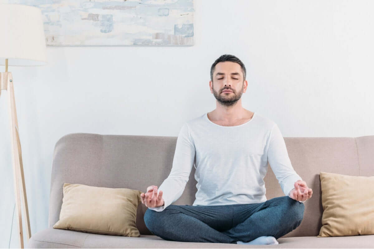 A man sitting cross-legged and meditating on a couch.
