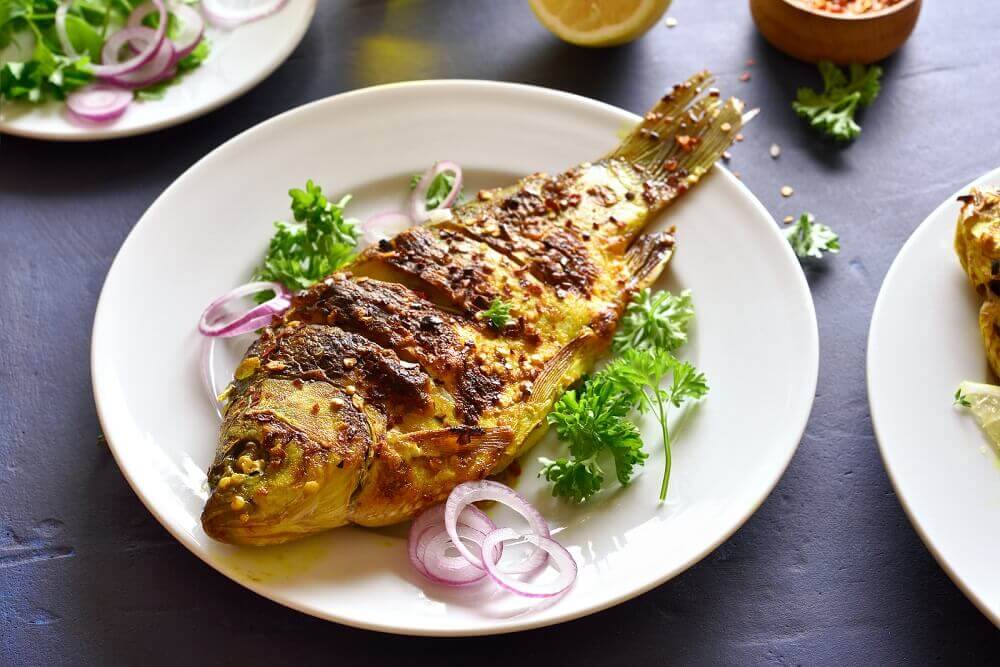 Cooked fish on a plate with parsley and red onions.