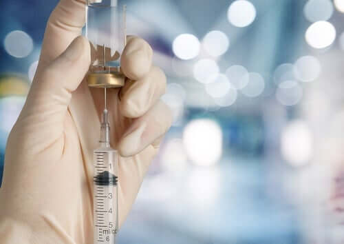 A hand with a glove removing liquid from a bottle with a needle and syringe.