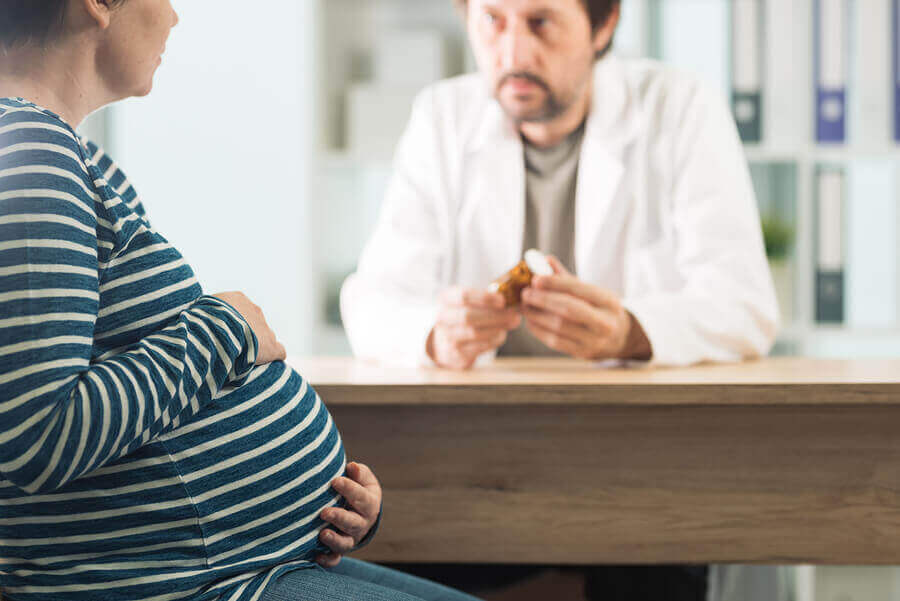 A doctor with a pill bottle in his hands talking to a pregnant patient.