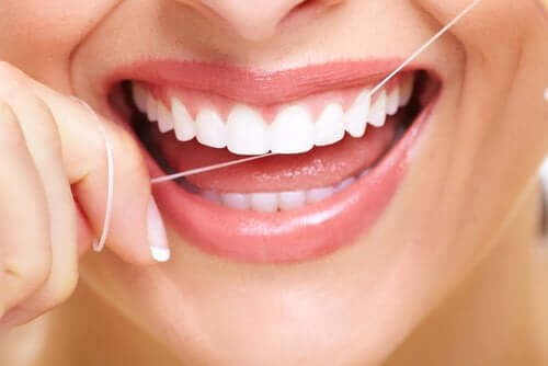 A woman smiling while she flosses her teeth.