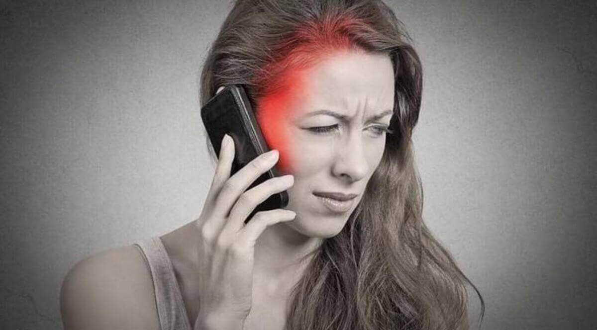 Kobieta z bólem głowy trzyma telefon komórkowy.