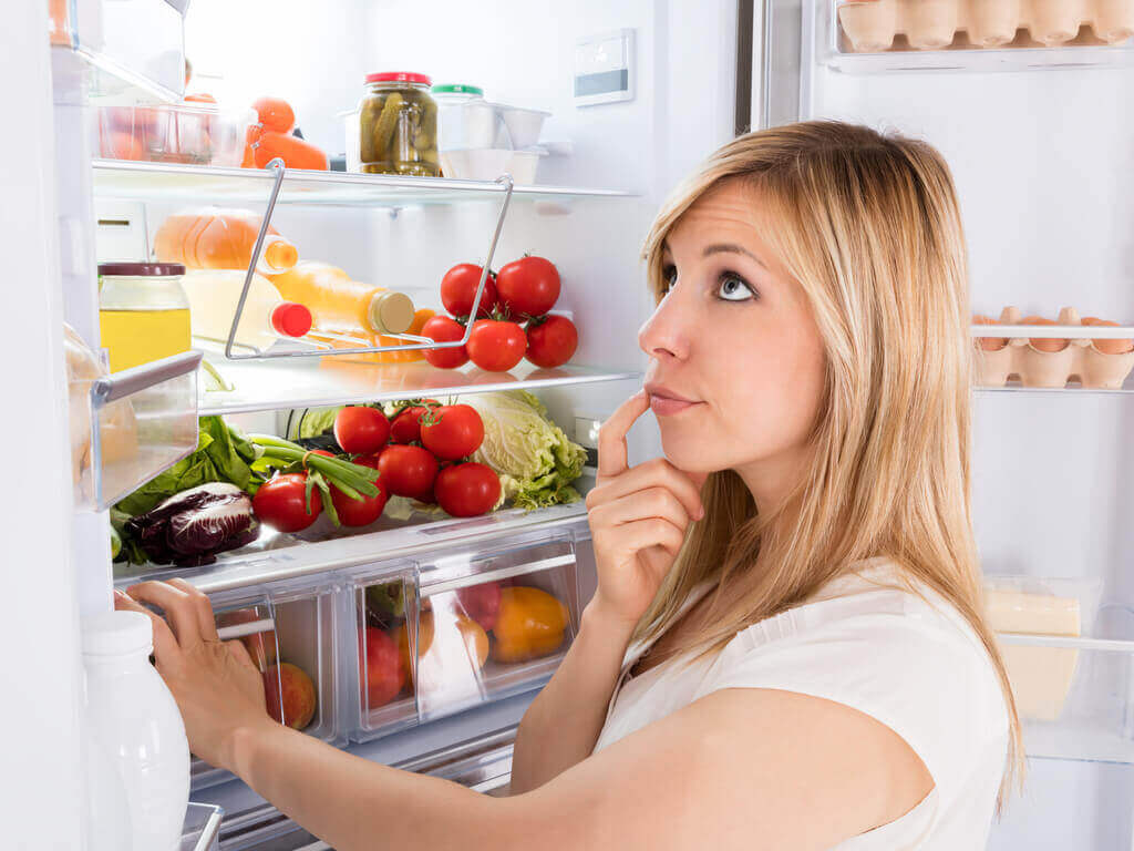 Mrożonki: wszystko, co powinieneś wiedzieć; kobieta stojąca przed lodówką myśląca o tym, co zjeść