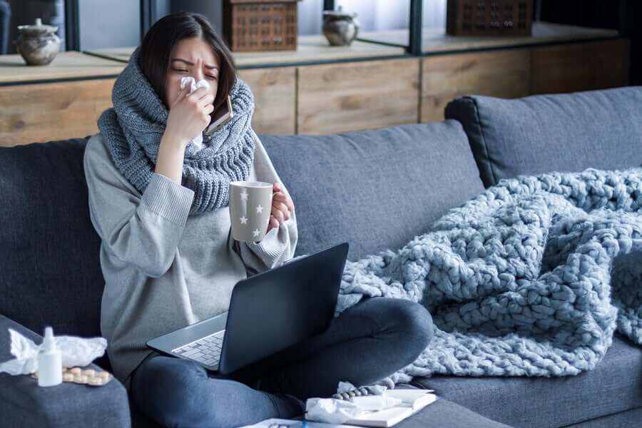 A woman with the flue sitting on a couch with a scarf wrapped around her neck.