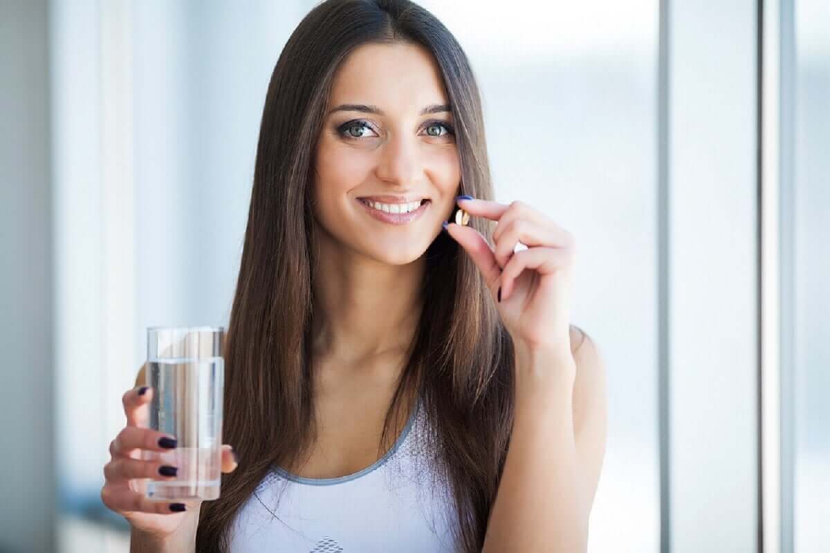 A woman holding two vitamins in one hand, and a glass of water in the other.