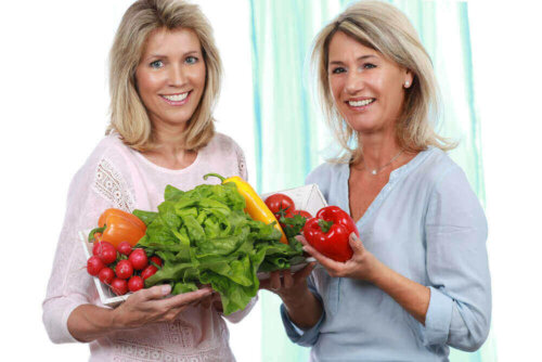 Two women holding fruit and vegetables.