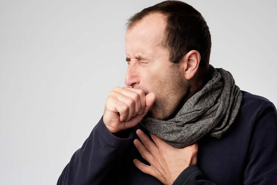 A man with a scarf around his neck, couphing and holding his chest.