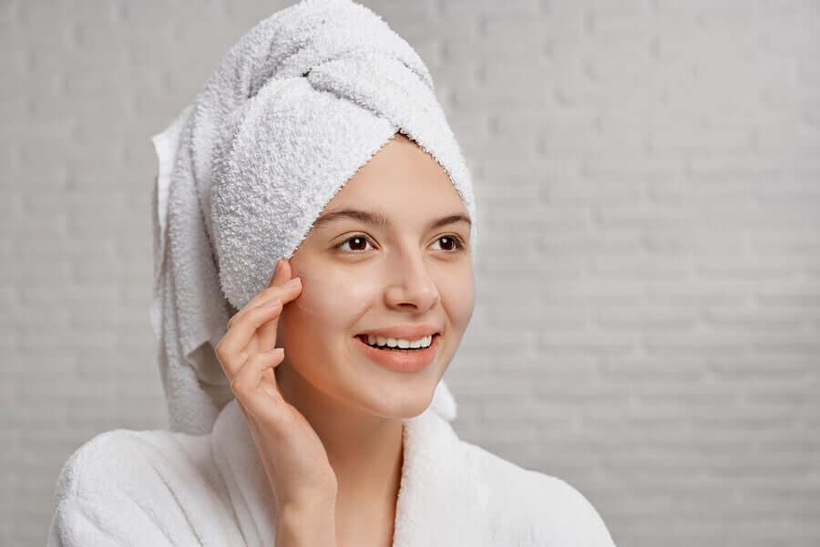 A woman rubbing lotion on her face after a shower.