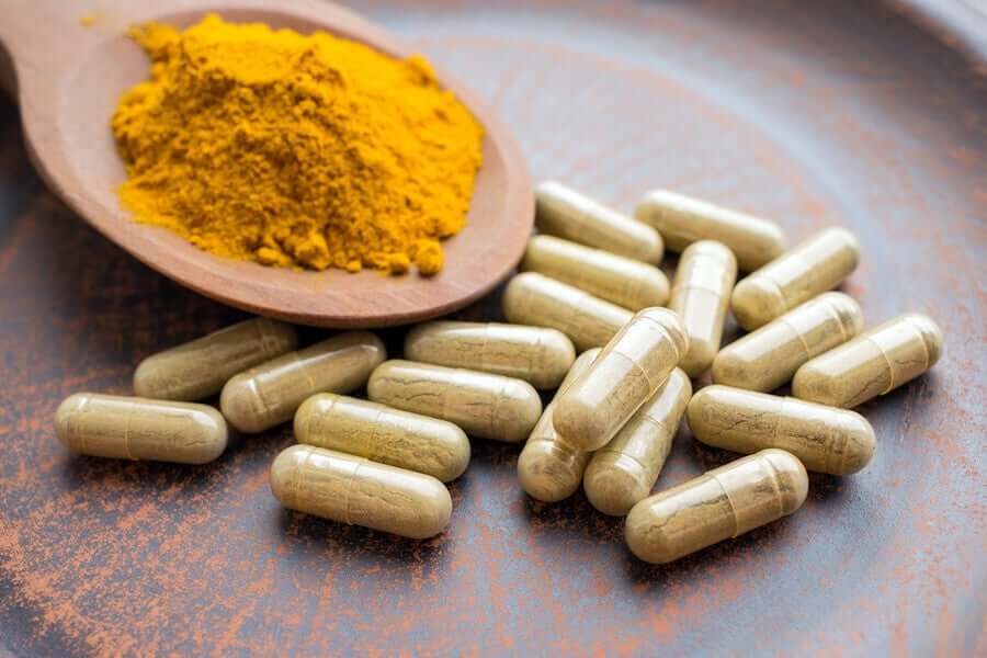 A wooden spoon full of turmeric powder on a plate of turmeric supplements.