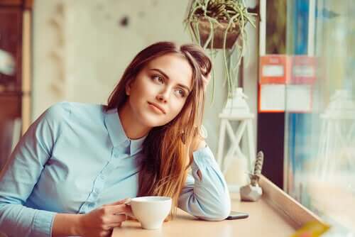 Kvinde med kaffe ser drømmende ud af vindue
